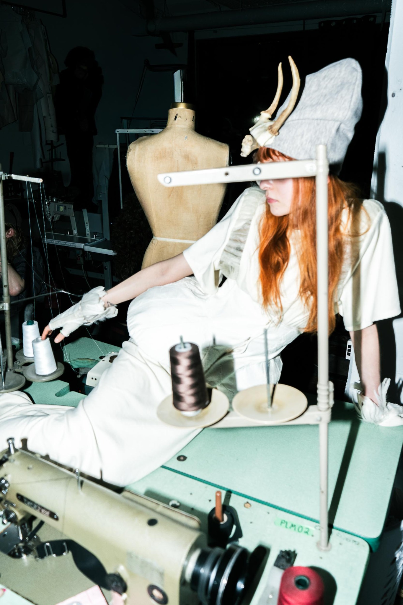 A designer wearing a sculptural horned headpiece works at an industrial sewing machine inside the LDF Studio.